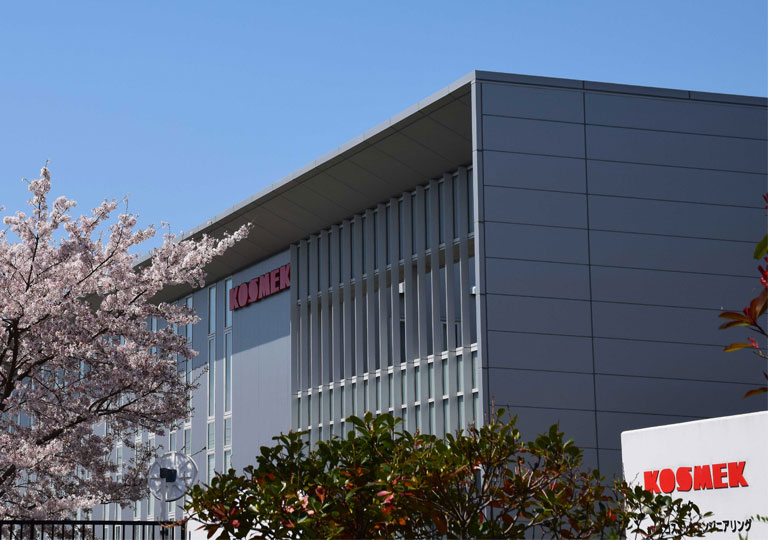 KOSMEK headquarters building in Japan surrounded by cherry blossoms, representing innovation and precision engineering.