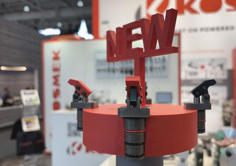 KOSMEK TQA mid-pressure compact clamps mounted on a red demo fixture with NEW sign at the trade show booth