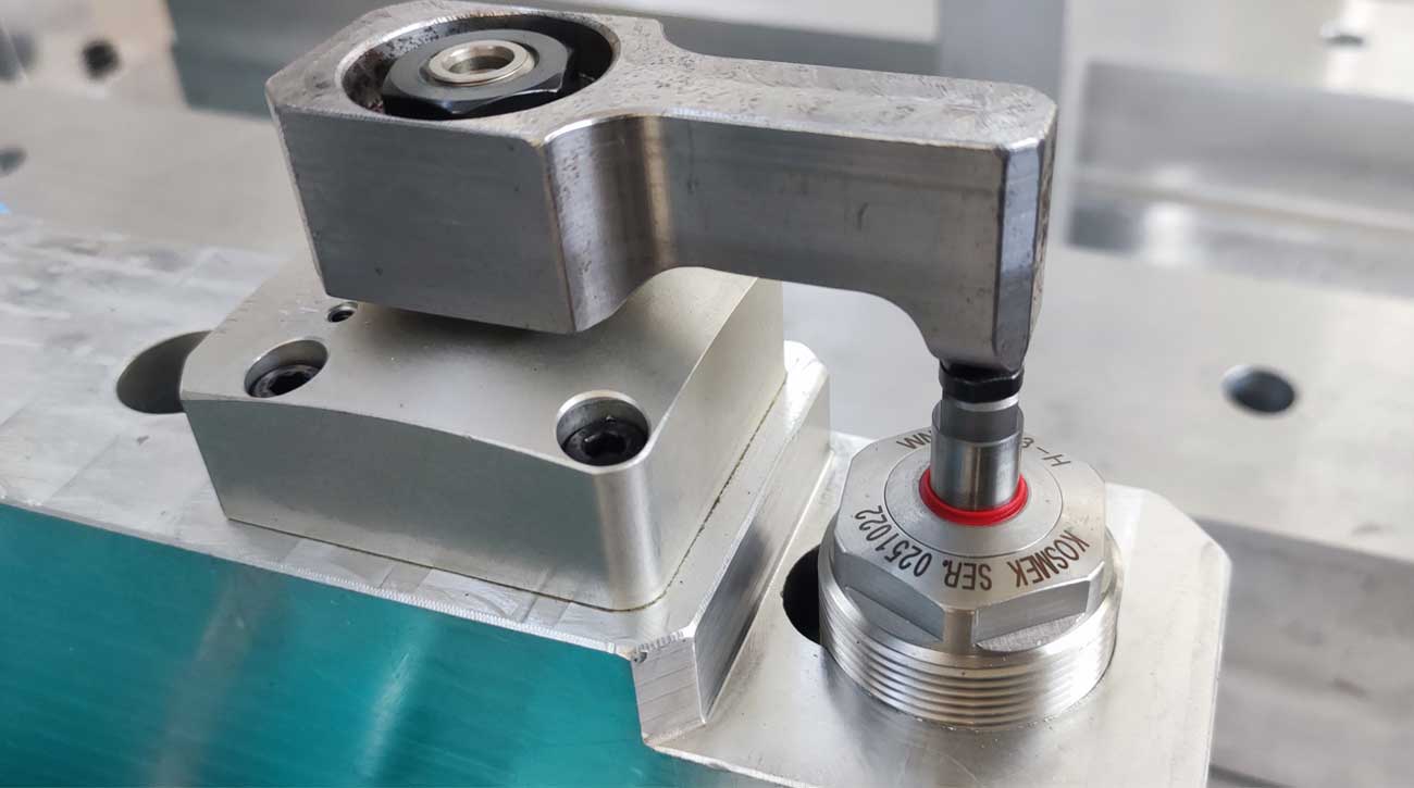 Nahaufnahme eines KOSMEK High-Power Pneumatik-Schwenkspanners und Abstützelements in einer IWAMET-Bearbeitungsvorrichtung für Aluminiumgussteile.