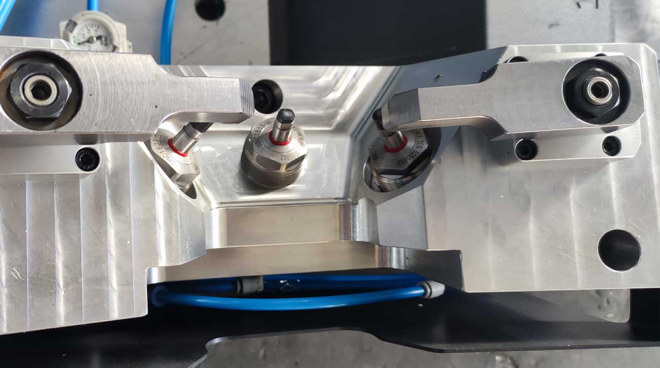 Draufsicht auf eine Bearbeitungsvorrichtung von IWAMET mit KOSMEK High-Power Pneumatik-Schwenkspannern und Abstützelementen zum Spannen von Aluminiumgussteilen.