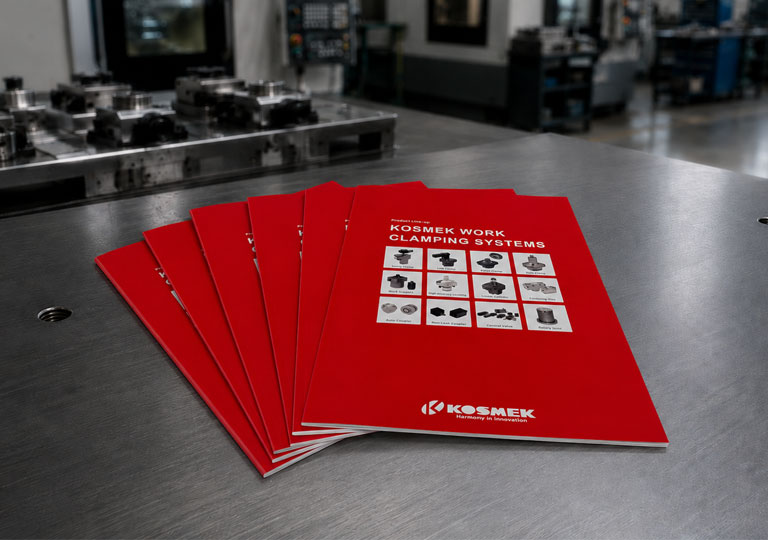 New KOSMEK Work Clamping Systems catalogs arranged on a metal worktable in a machining factory.